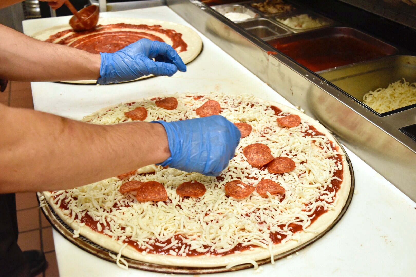 Photo of a man placing pizza toppings on a pizza