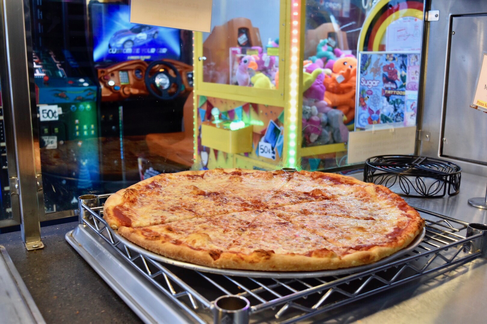 Photo of a cheese pizza in front of some arcade machines